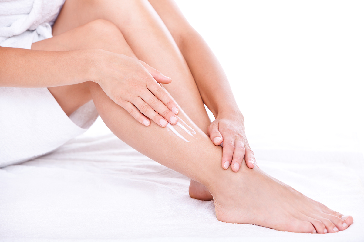 Woman applying moisturizer cream on the legs over white background